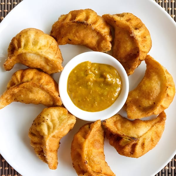 Golden-brown fried momos arranged in a circle around a small bowl of green chutney on a white plate.