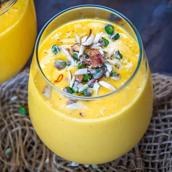Close-up of a vibrant yellow mango lassi, garnished with pistachios, almonds, and saffron threads.