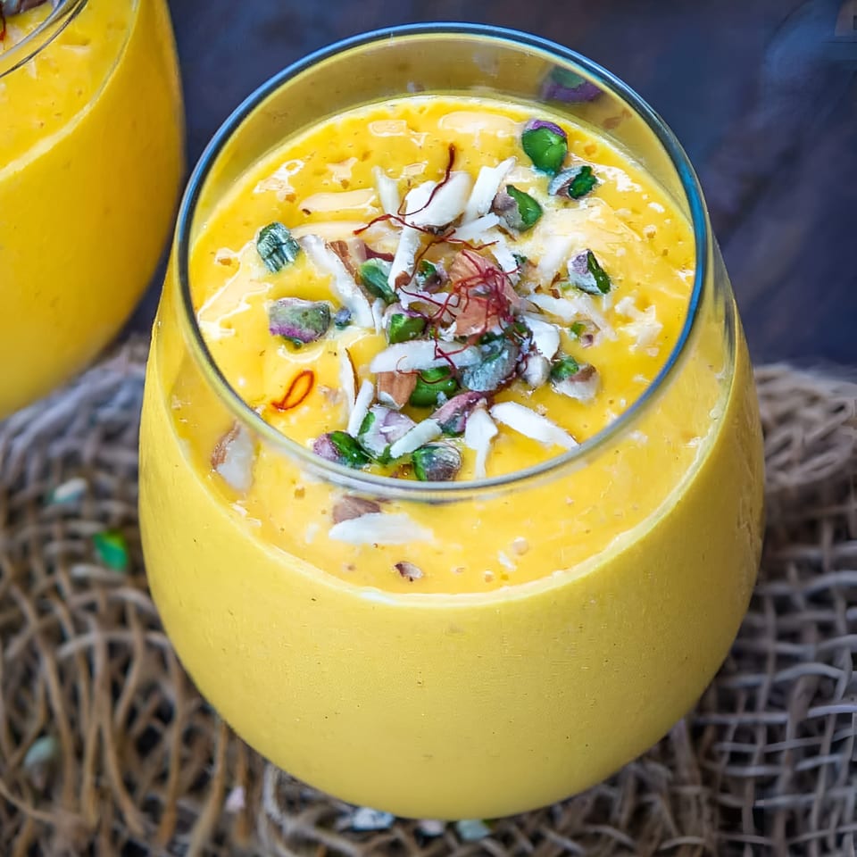 Close-up of a vibrant yellow mango lassi, garnished with pistachios, almonds, and saffron threads.