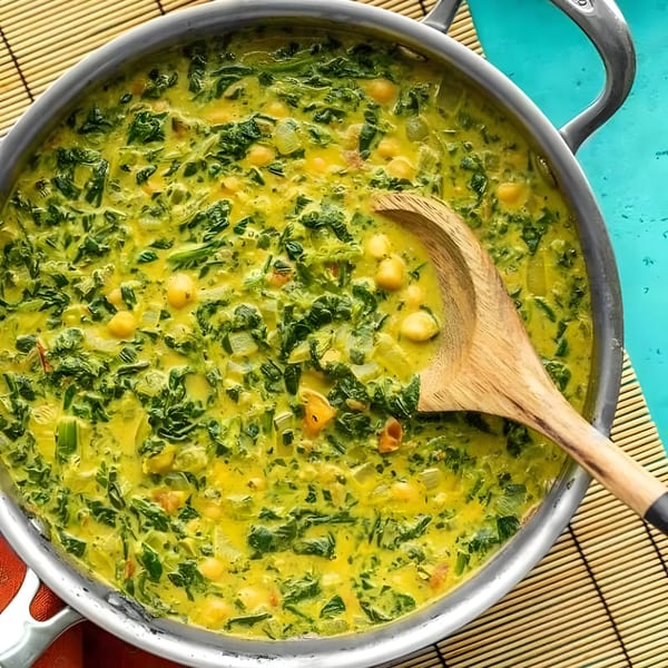 A large pot of vibrant green Indian saag with chickpeas and a wooden spoon.