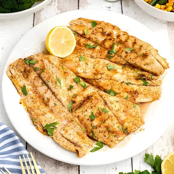 Indian spiced fish fillets with lemon and parsley on a white plate.